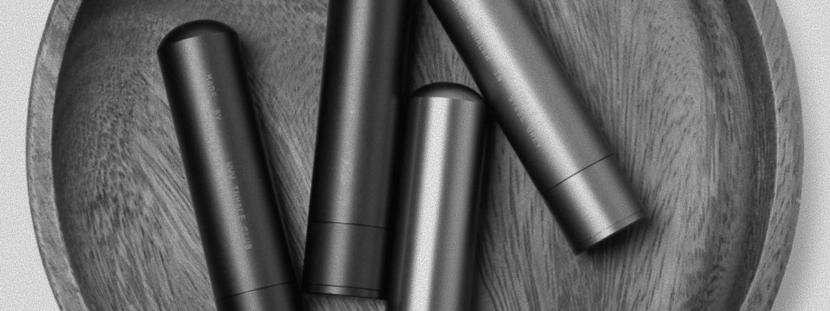 Black and white image of four sleek, cylindrical aluminium inhalers from Inhale Club, arranged on a textured wooden surface.