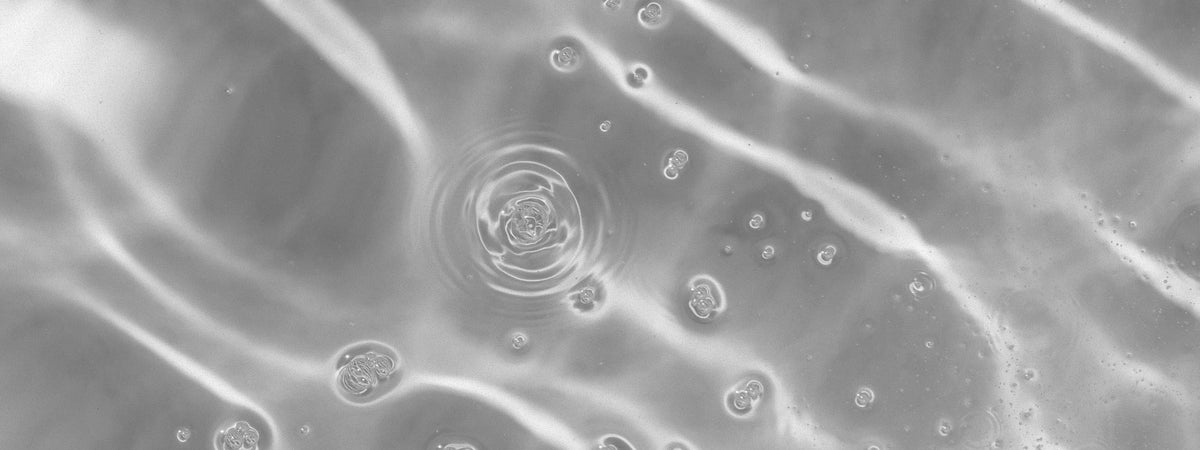 A single ripple spreading across water dotted with bubbles, black and white