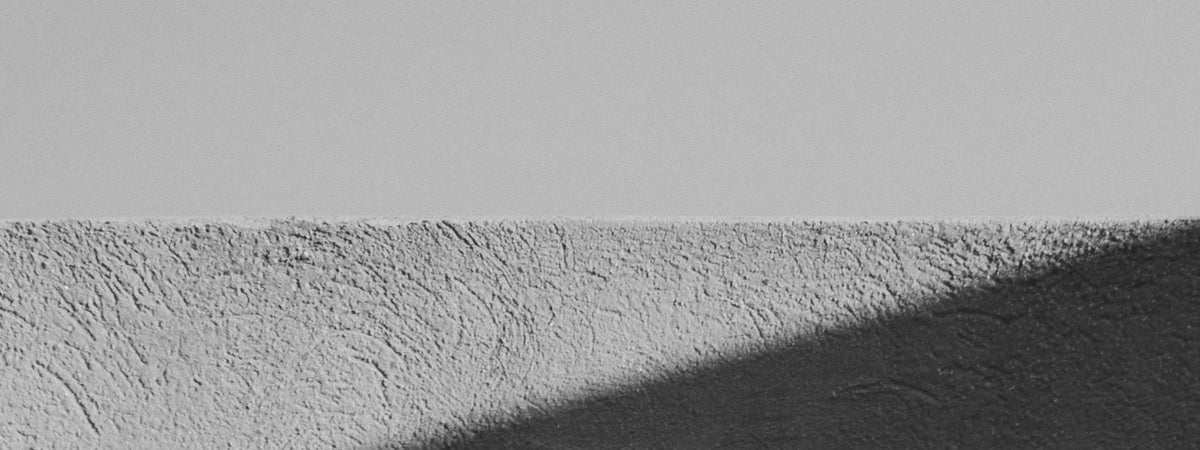 A hard diagonal shadow falling across a textured wall, black and white